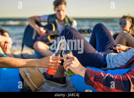 Primo piano delle mani bicchieri tintinnanti di bottiglie di birra sulla spiaggia Foto Stock