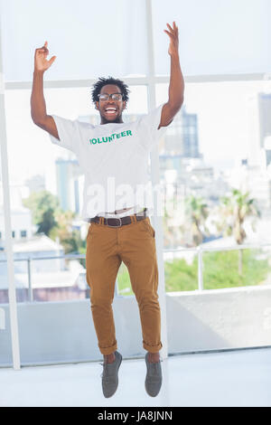 L'uomo jumping con volontario tshirt quindi solleva le braccia in un ufficio moderno Foto Stock