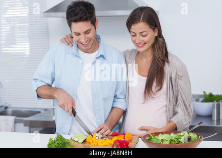 L uomo come tagliare le verdure accanto al suo partner preganant in cucina Foto Stock