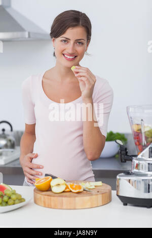 Donna incinta di mangiare un'uva durante la preparazione di un cocktail di frutta Foto Stock