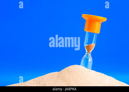 Clessidra in piedi nella sabbia su sfondo blu con spazio di copia Foto Stock