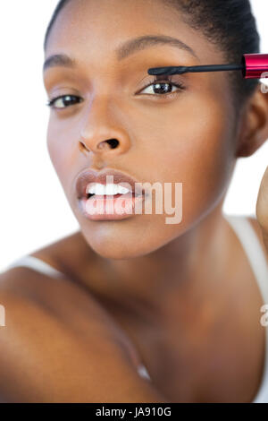 Giovane donna con mascara per le sue ciglia su sfondo bianco Foto Stock