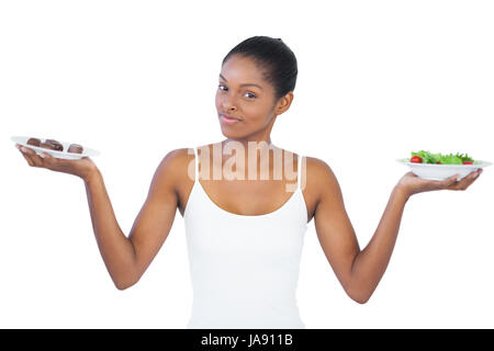 Bella donna di decidere di mangiare in modo sano o non è su sfondo bianco Foto Stock