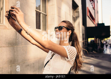 Registrazione Vlogger contenuto per il suo viaggio vlog. Giovane donna prendendo selfie in una strada utilizzando una fotocamera digitale. Foto Stock