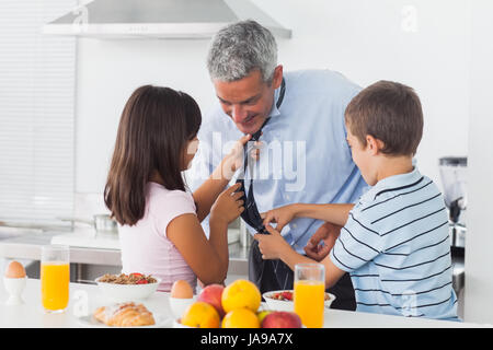 I bambini che fissa i loro padri cravatta in cucina a casa Foto Stock