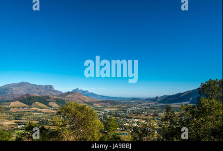 Una vista del paesaggio di Franschhoek vino regione valle su un luminoso bleu sky giornata soleggiata con montagne in lontananza Foto Stock