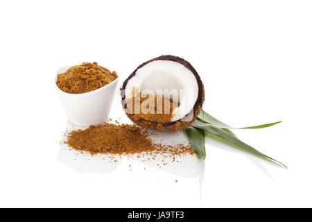 Lo zucchero di cocco sfondo. Sana alternativa di zucchero. Metà di noce di cocco, foglie di palma e cocco marrone zucchero isolato su sfondo bianco. Foto Stock