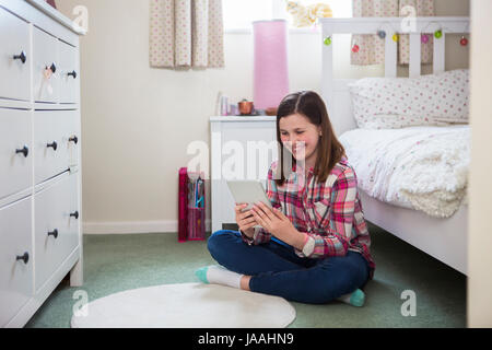 Ragazza seduta sul pavimento della camera da letto con tavoletta digitale Foto Stock