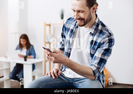 Tenere il passo con le notizie. Interesse positivo affascinante uomo con il suo smartphone per la verifica degli aggiornamenti sul suo profilo di rete sociale e la lettura di alcune notizie Foto Stock