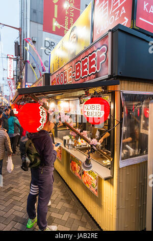 Osaka, Dotonbori. Notte tempo. Vista lungo manzo di Kobe contatore da asporto con persone ordinare del cibo. Red chochin lanterne di carta appeso. Foto Stock