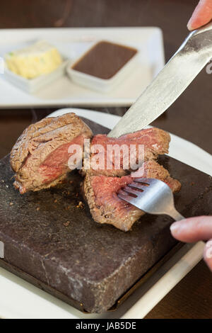 Mezzo raro bistecca sfrigolante su pietra calda piastra essendo tagliate a fette servita nel ristorante elegante Foto Stock