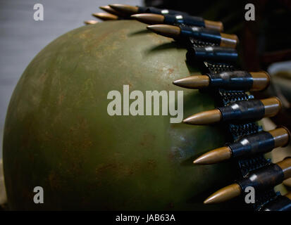 Macchina cinghia pistola con proiettili sul vecchio casco verde Foto Stock