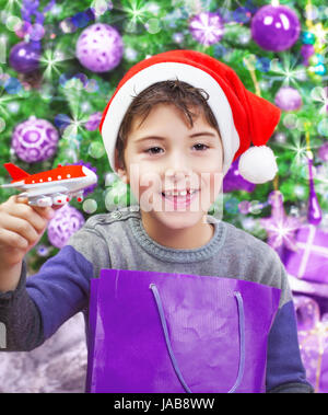 Ritratto di carino ragazzo arabo godendo di Natale regalo, giocando con un piccolo aeroplano di plastica, indossando red Santa hat, decorate albero di Natale, Capodanno Foto Stock