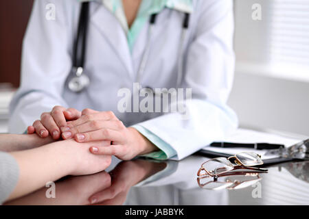 Gentile Dottore femmina mani tenendo la mano del paziente seduto alla scrivania di incoraggiamento, empatia, tifo e supporto durante la visita medica. Foto Stock