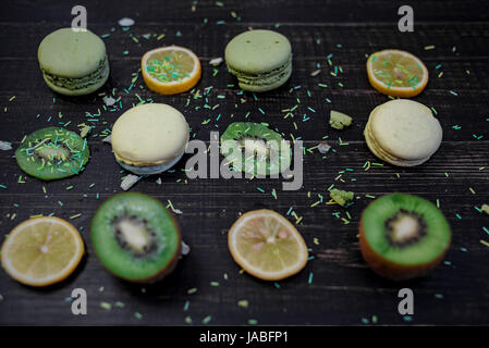 Verde e bianco amaretti con kiwi, arancio e limone in ordine su un legno scuro tabella Foto Stock