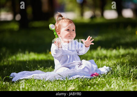 Carino baby ragazza seduta sul prato verde nel parco della città a caldo giorno d'estate. Foto Stock