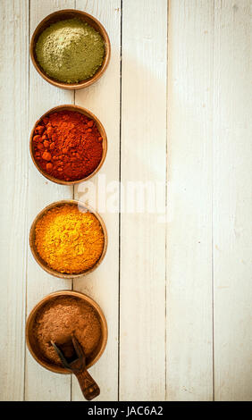 Confine di spezie colorate disposte in una fila verticale con peperoncino, curry, pepe rosso e matcha in polvere in piccole ciotole su uno sfondo del dipinto di bianco per le schede con copyspace Foto Stock