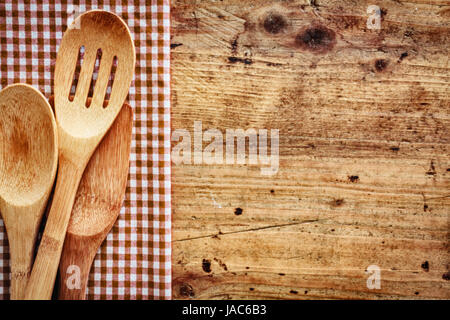 Sfondo di legno con copyspace delimitata da un punto rosso e bianco paese panno con cucina in legno utensili giacente su di esso Foto Stock