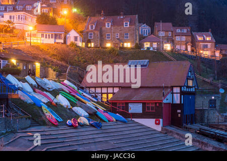 Grazioso e pittoresco villaggio costiero (vista serale) sono accese in località case e barche colorate sono su uno scalo - Runswick Bay, Yorkshire, Inghilterra, Regno Unito. Foto Stock