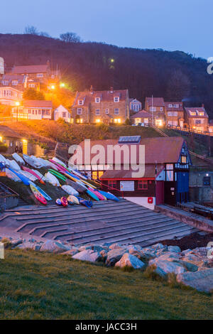 Grazioso e pittoresco villaggio costiero (vista serale) sono accese in località case e barche colorate sono su uno scalo - Runswick Bay, Yorkshire, Inghilterra, Regno Unito. Foto Stock