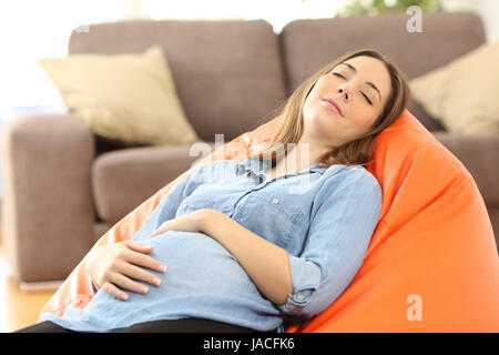 Ritratto di una stanca donna incinta di dormire su un pouf nel salotto di casa Foto Stock