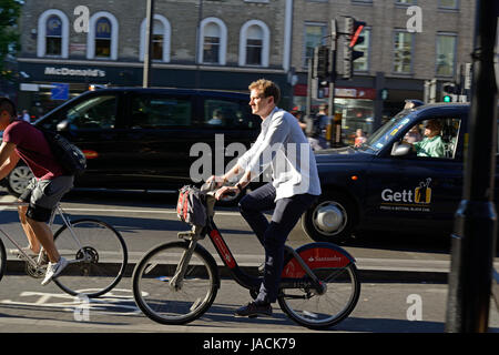 Uomo a cavallo di un Santander noleggio elettrico bicicletta pedalando attraverso Kings Cross, London, nelle ore di punta Foto Stock