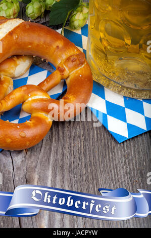 Ein Glas mit Bier, Brezeln und einige Hopfendolden auf einem alten rustikalen Holztisch Mit einem blauen Banner mit der Aufschrift Oktoberfest Foto Stock