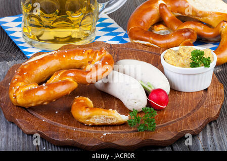 Rundes Holzbrett mit salsiccia bianca, Brezel, Senf und Radieschen und einem Glas mit Bier auf einem alten rustikalem Holztisch Foto Stock