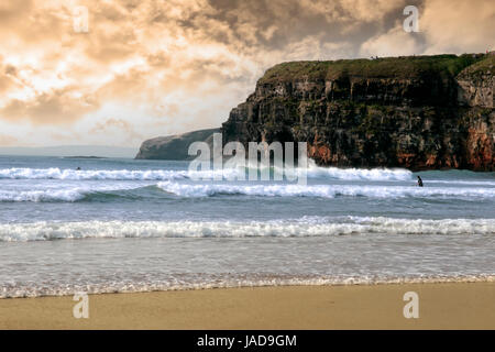 Bella pulita oceano Atlantico con surfers cattura le onde con scogliere in background sulla costa dell'Irlanda Foto Stock