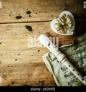 Immagine concettuale della notte di Natale di musica con un registratore di flauto giacente su un vecchio punteggio musicale al fianco di una decorazione a forma di cuore dono con un inchino ornamentali, copyspace sul legno rustico sfondo Foto Stock