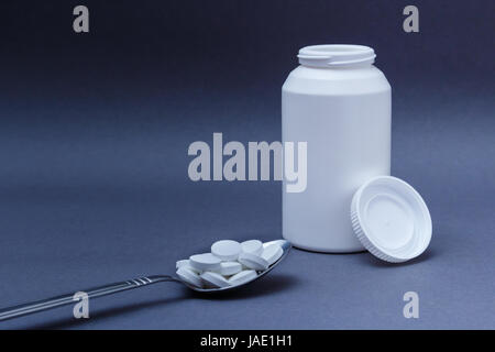 White pillole di medicina in cucchiaio di acciaio e bottiglia dietro Foto Stock