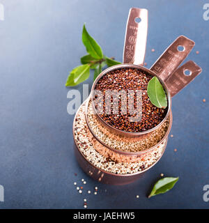 Pila di rame tre tazze di misurazione con un misto di materie di quinoa, sud americana di grano, baia con foglie di alloro su sfondo blu. Sana e senza glutine f Foto Stock