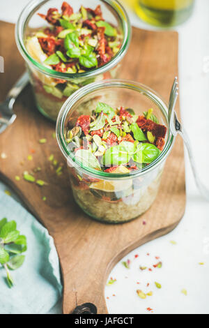 Vegano sana insalata con quionoa, avocado, pomodori secchi, basilico, olio d'oliva, menta in vasetti di vetro, Sfondo marmo, il fuoco selettivo. Pulire mangiare, sup Foto Stock