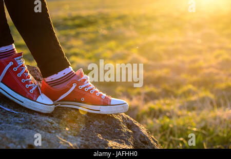 Piedi in sneakers contro lo sfondo del sole di setting Foto Stock