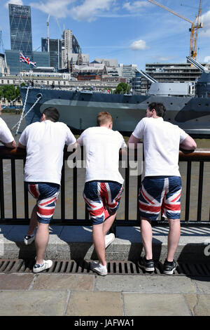 Giovani uomini che indossano Unione Jack shorts nella parte anteriore del dispositivo HMS Belfast, Londra Summer 2017 REGNO UNITO Foto Stock