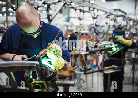 Maschio esperto lavoratore in fabbrica utilizzando attrezzi di saldatura su di un telaio di bicicletta in una fabbrica. Foto Stock