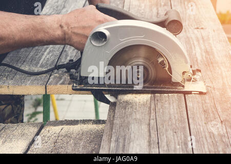 Maschio di tagli a mano con una sega circolare un pezzo di cartone in una giornata di sole. Tonica. Foto Stock