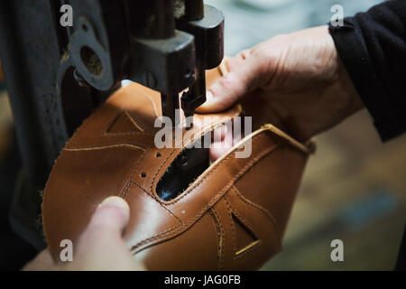 Chiusura del lavoratore in un calzolaio di officina, utilizzando una macchina per la foratura dei fori in una scarpa in cuoio. Foto Stock