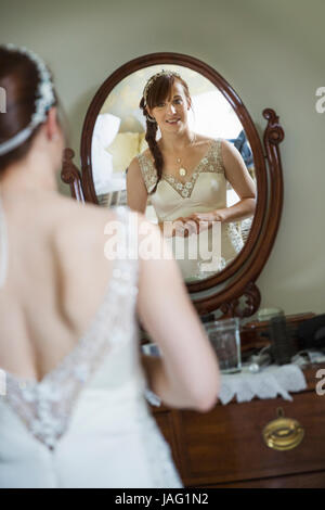 Sposa sorridente nel suo abito da sposa guardando a se stessa in uno specchio. Foto Stock