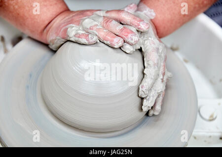 Una persona che utilizza una rotazione ruota in ceramica per gettare un vaso utilizzando argilla, mani lo stampaggio della creta bagnata. Fase iniziale di gettare una pentola. Foto Stock