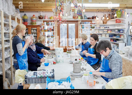 Un gruppo di persone sedute su un banco da lavoro in un laboratorio di ceramiche, costru zione oggetti di creta. Una donna con una tazza di tè. Foto Stock