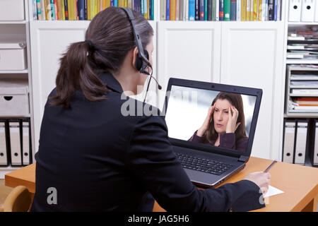 Donna con cuffie di fronte il suo laptop a scrivere qualcosa su un foglio di carta mentre si effettua una chiamata video attiva con un paziente o un client, spazio di copia Foto Stock