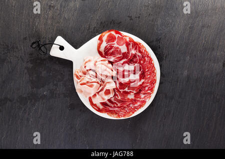 Assortimento di vari affettati snack. Servire freddo antipasti italiani su un marmo bianco tagliere su nero pietra naturale da ardesia Foto Stock