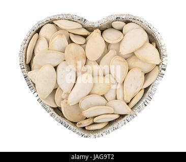 Vista dall'alto di tostati e salati semi di zucca il riempimento di un cuore a forma di coppa di stagno isolato su uno sfondo bianco. Foto Stock