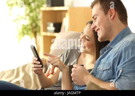 Coppia felice il controllo di una smart phone seduta su un divano nel salotto di casa Foto Stock