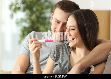 Felice coppia controllo test di gravidanza seduta su un divano nel salotto di casa Foto Stock