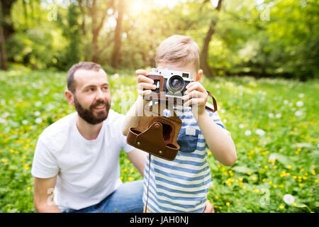 Giovane padre con piccolo ragazzo con telecamera in estate park. Foto Stock