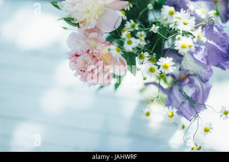 Bouquet di peonie bianco, chamomiles e iride fiori in vaso di vetro. Estate sfondo. Foto oscurata Foto Stock