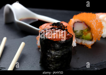 Pezzi di sushi con salsa di soia in ardesia, bassa fotografia di chiave ma con colori vivaci su sfondo nero Foto Stock