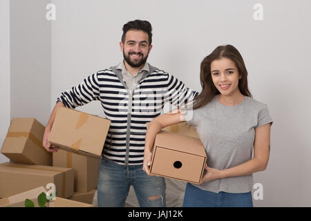 Attraente coppia giovane è in movimento, sorridente e scatole di contenimento mentre in piedi tra spacchettato caselle. Foto Stock